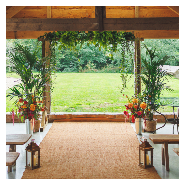 Living plant ceremony backdrop framing an outdoor garden view, surrounded by palms and The Haybarn in Hereford.
