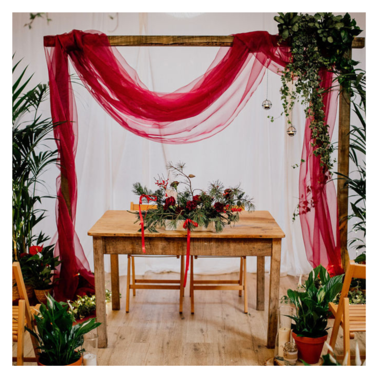 Wedding ceremony backdrop with burgundy draping, living greenery and potted plants at The Haybarn