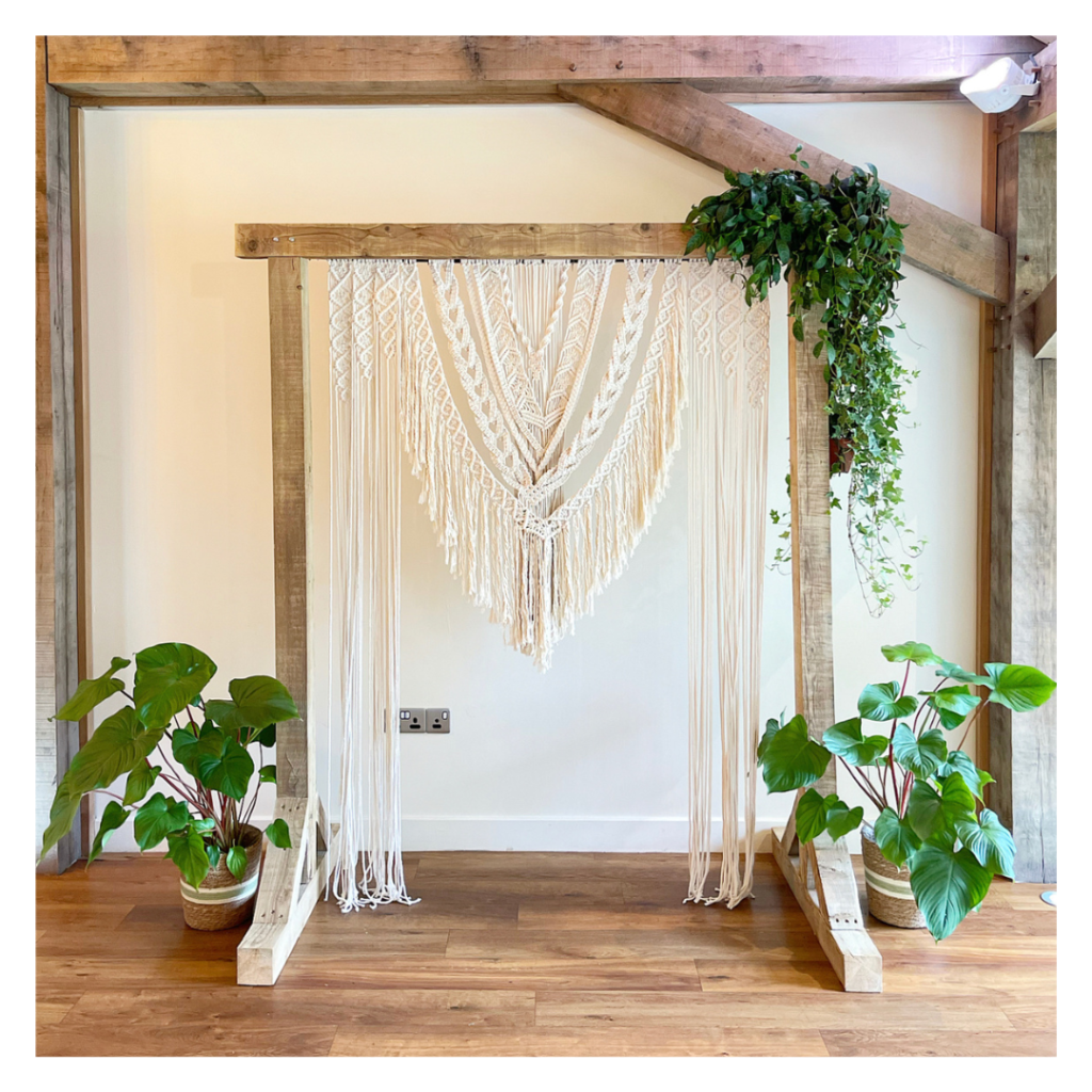 Boho wedding ceremony backdrop with macramé hanging, wooden frame and trailing greenery at Bredenbury Court, Hereford.