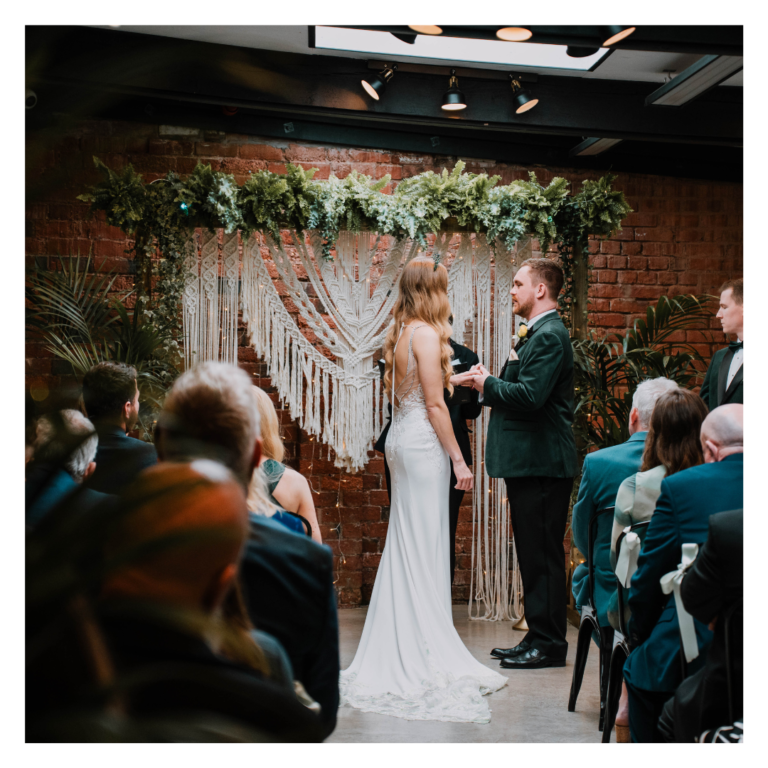 Couple exchanging vows in front of a lush living plant wedding backdrop at The Shack Revolution