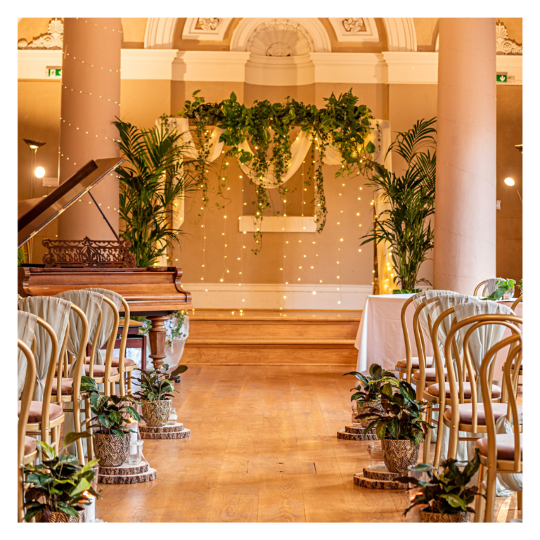 Wooden wedding ceremony backdrop styled with trailing living plants and aisle greenery at The Lion Ballroom