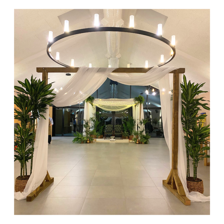 Mandap 15 Botanical mandap entrance with wooden frame, white draping and greenery leading to a Hindu wedding ceremony space