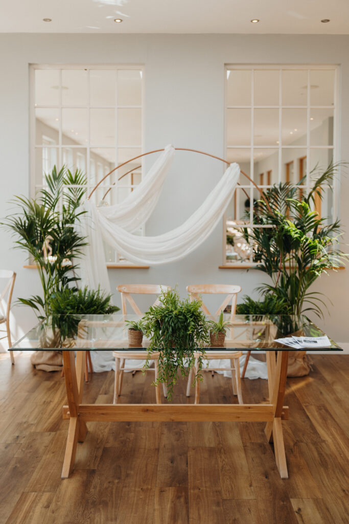 Living plant wedding ceremony backdrop with rose gold hoop, flowing white drapes and tropical plants, creating a botanical wedding focal point for indoor ceremonies.