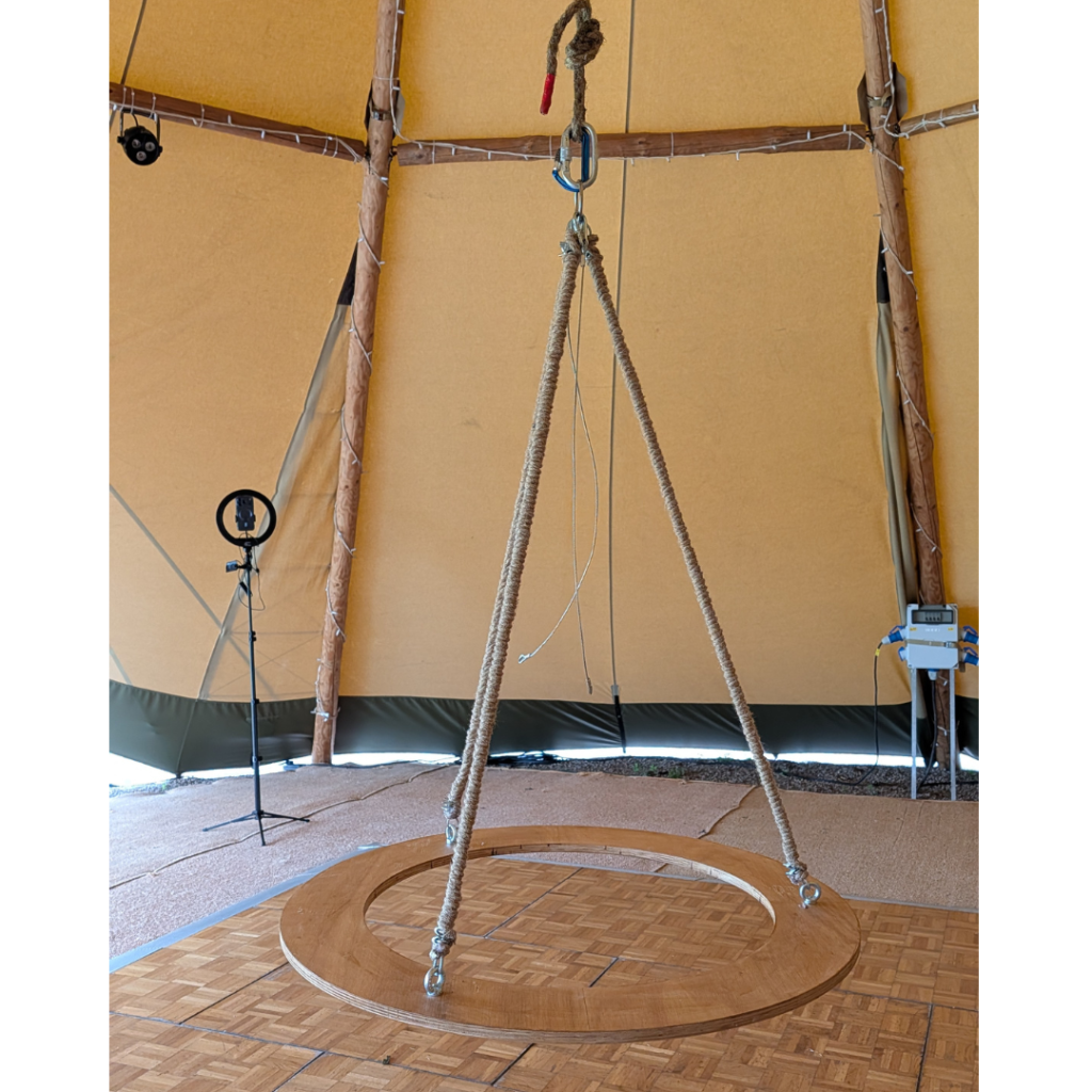 Handcrafted wooden wedding chandelier structure suspended inside a tipi venue, featuring a central disco ball ready for a botanical hanging installation.