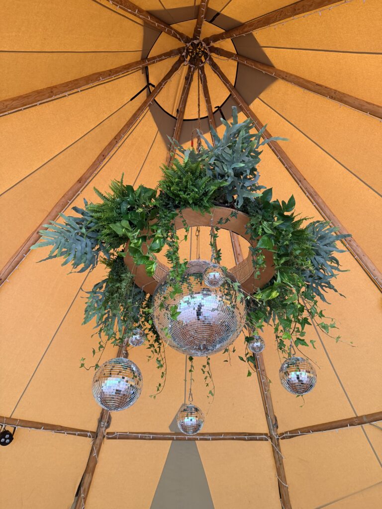 Botanical wedding chandelier with disco balls, trailing greenery and hanging plants, creating a unique focal point for a modern wedding venue.