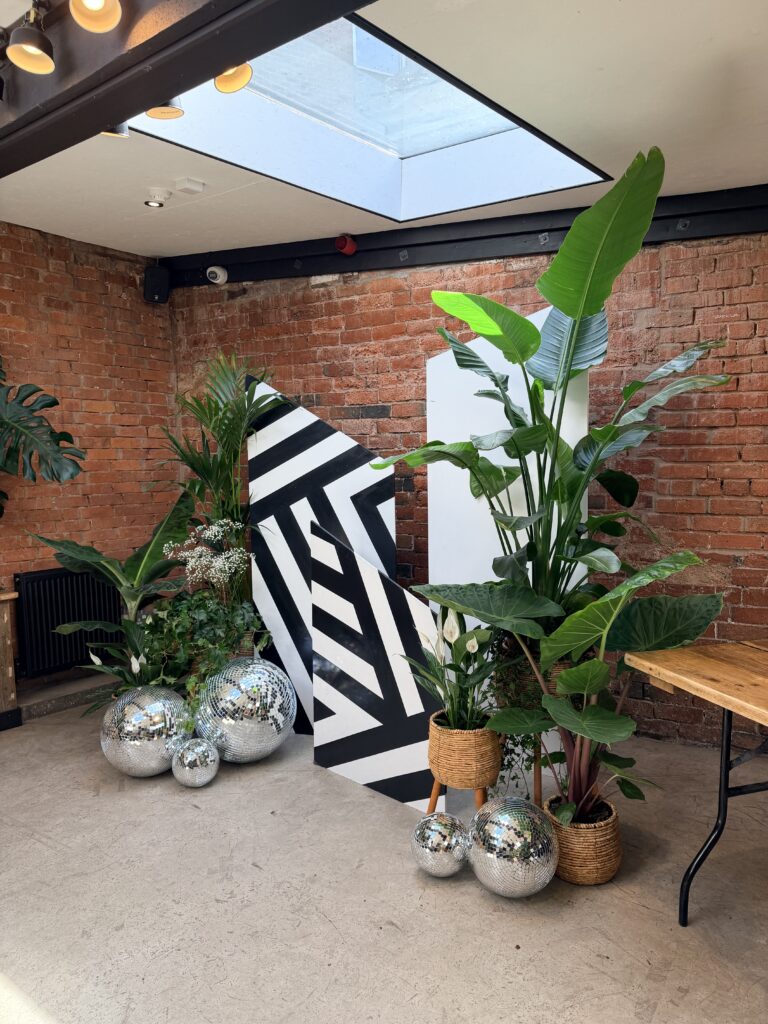 Disco balls line the floor of this ceremony backdrop with living plants.