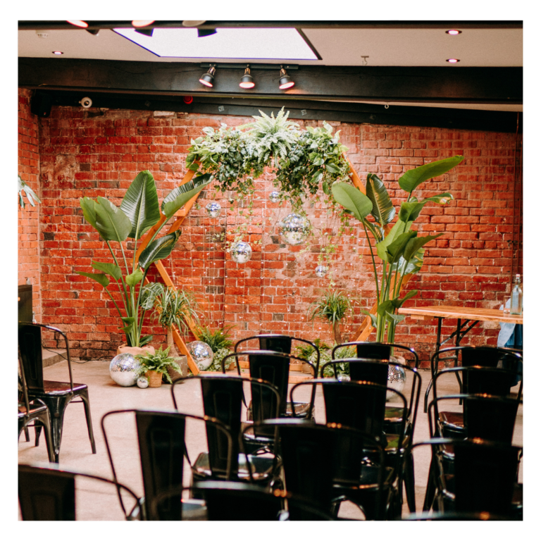 Hexagon wedding ceremony backdrop with tropical plants, hanging disco balls and trailing ivy, creating a modern botanical wedding focal point with living plant décor.