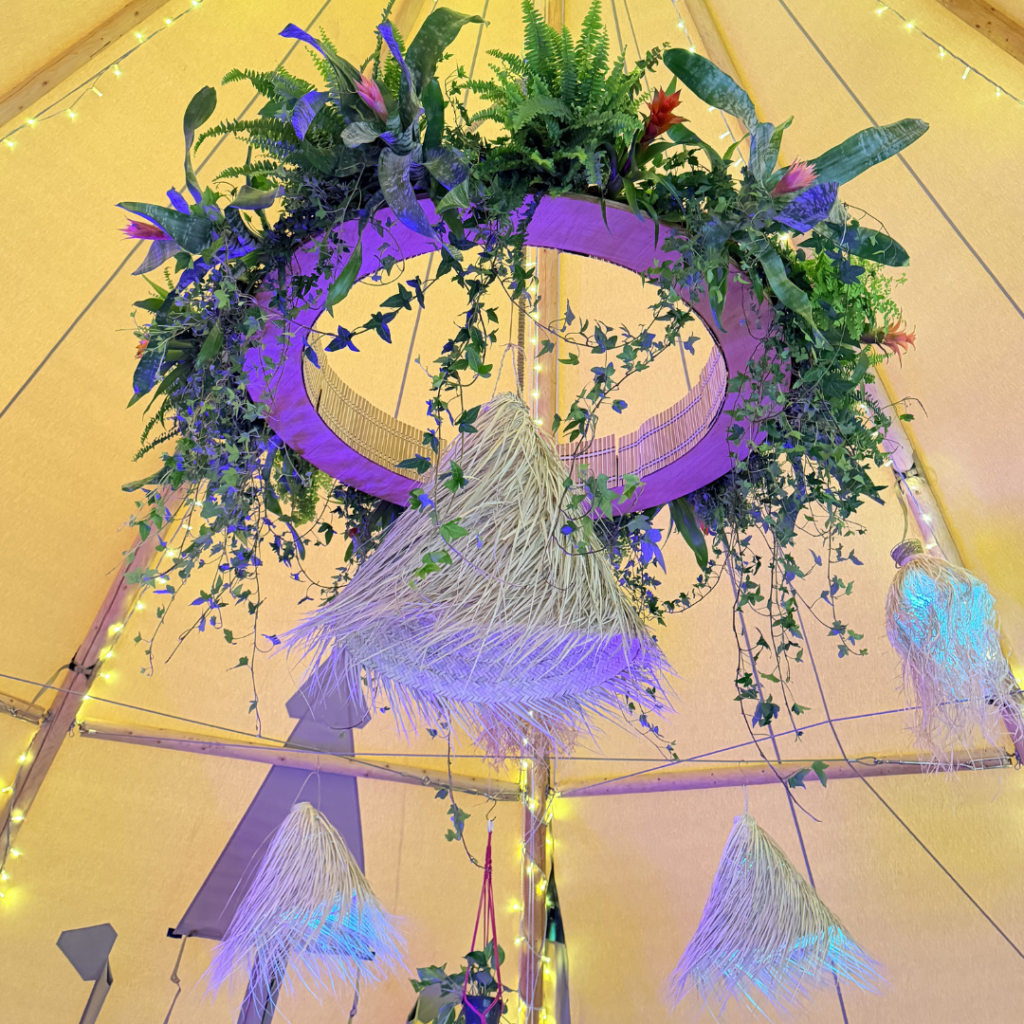 Large hanging plant chandelier suspended inside a wedding teepee, featuring lush greenery and macramé details for a statement botanical installation.