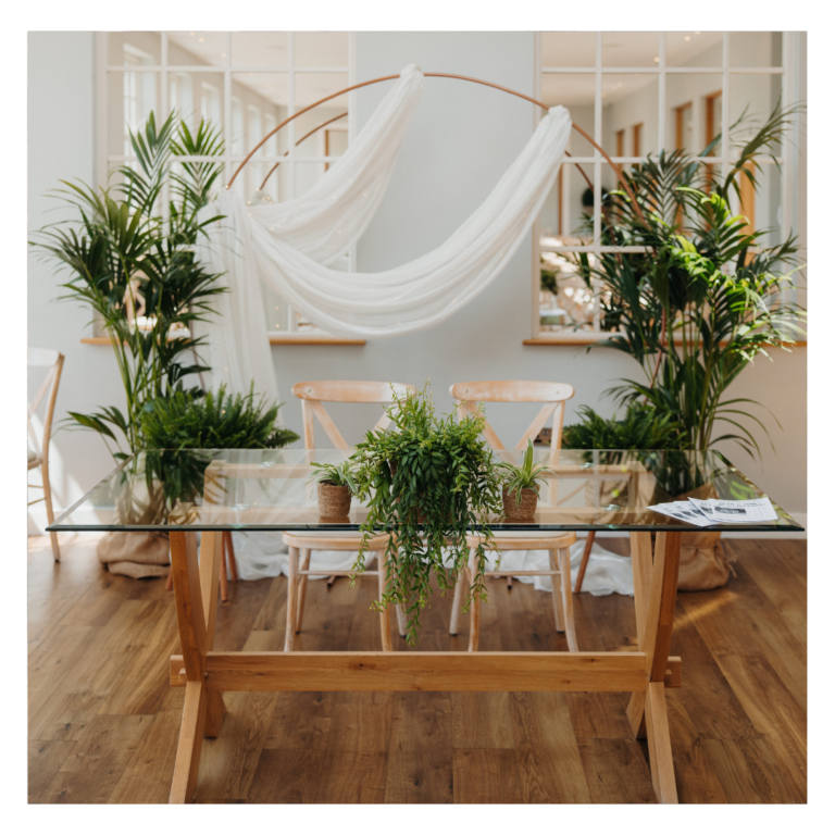 Living plant wedding ceremony backdrop with rose gold hoop, flowing white drapes and tropical plants, creating a botanical wedding focal point for indoor ceremonies.
