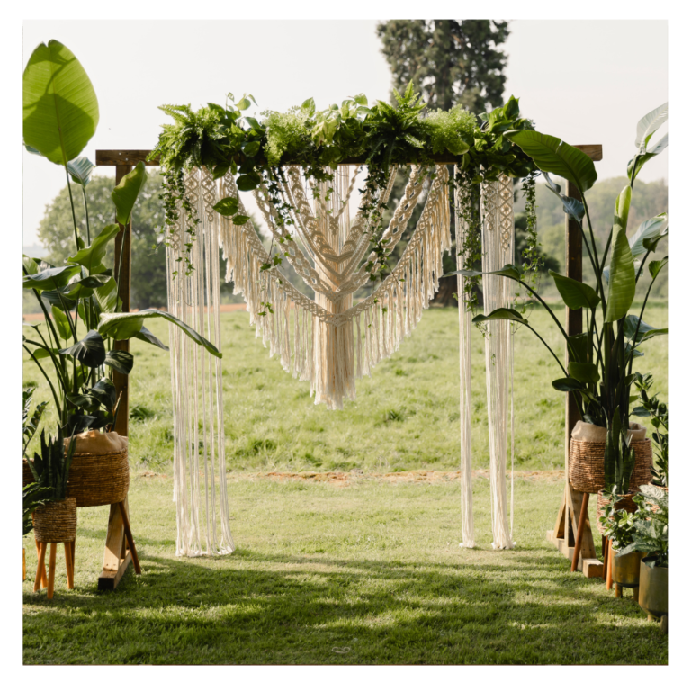 Outdoor wedding ceremony backdrop with macramé installation, tropical plants and cascading greenery for boho botanical wedding styling.