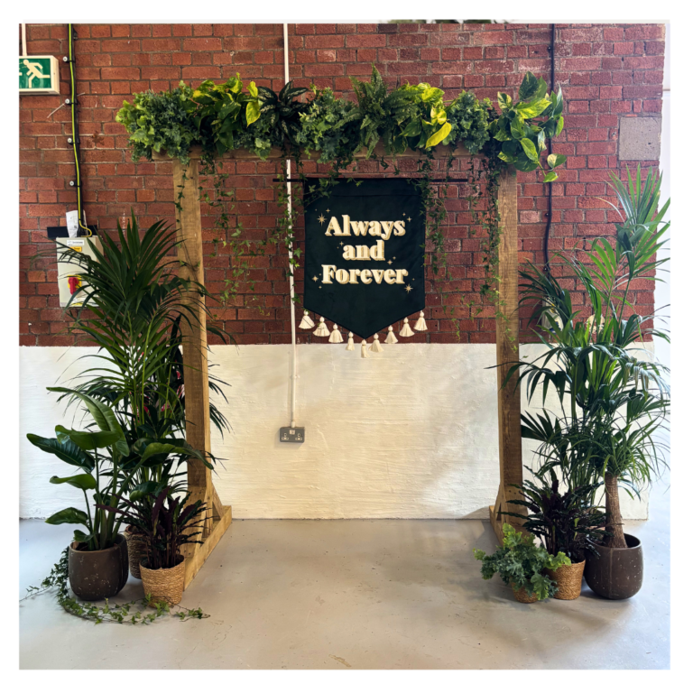 Wedding welcome sign backdrop with tropical plants, trailing ivy and botanical styling creating a statement entrance display for wedding guests.