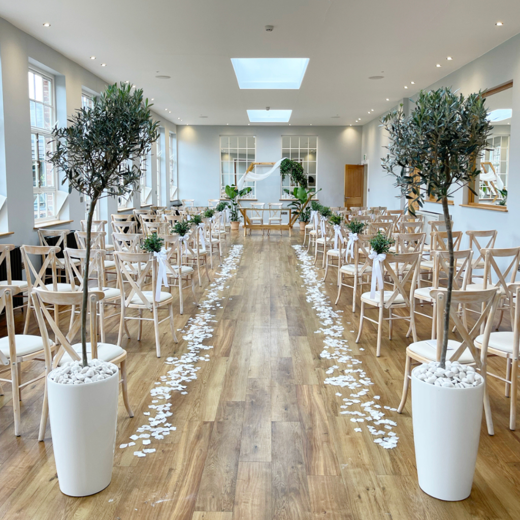 Wedding ceremony aisle lined with olive trees and living plants, creating a romantic botanical aisle for an indoor wedding ceremony.