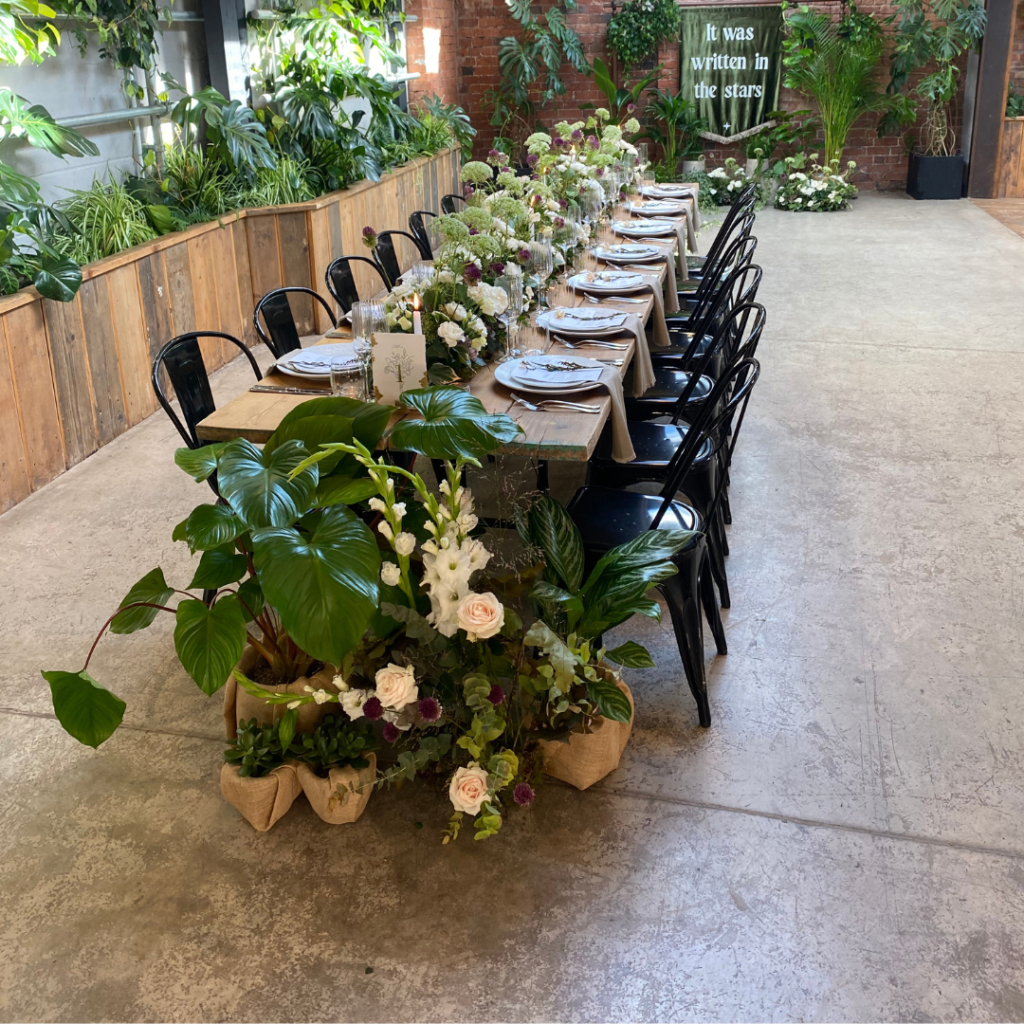 Long banquet wedding tables finished with large tropical plants and floral arrangements creating luxury botanical wedding styling.