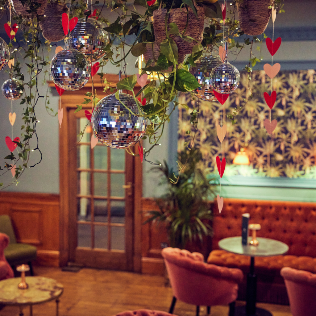 Luxury hanging botanical installation with trailing greenery and lanterns above banquet tables for elegant wedding styling.