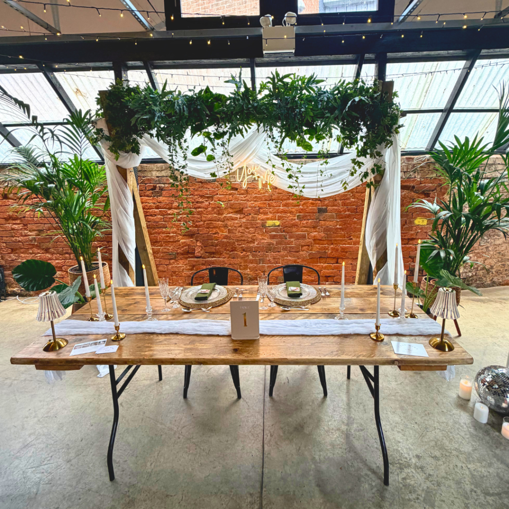 Top wedding table framed by a living foliage backdrop, candles and tropical plants creating a stunning botanical reception feature.