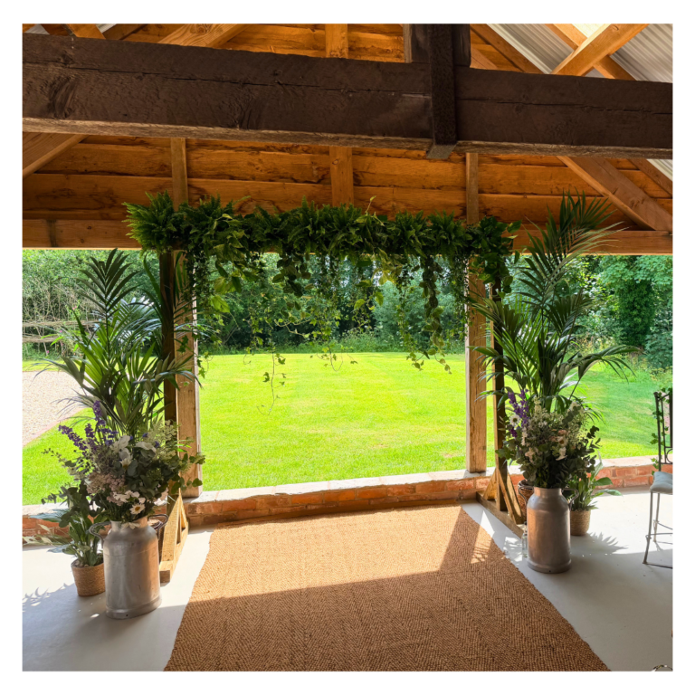 Living plant wedding backdrop framing a garden view with palms and trailing greenery at The Haybarn Hereford.