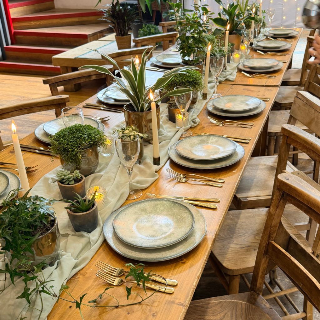 Long banquet wedding table styled with small living plant centrepieces, greenery, candles and place settings.